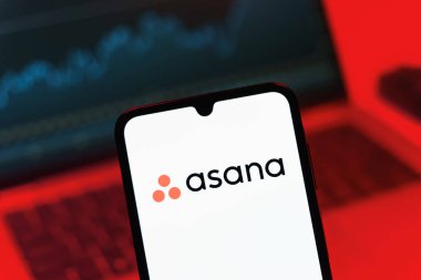 Prag, Çek Cumhuriyeti - 08 12 2025: Bilgisayarın önünde duran bir cep telefonu Asana logosunu gösteriyor. Asana görev yönetimi ve takım işbirliği için bir platformdur..
