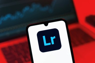Prag, Çek Cumhuriyeti - 08 12 2025: Dizüstü bilgisayarın önünde duran bir cep telefonu Lightroom logosunu gösteriyor. Lightroom fotoğraf düzenleme ve yönetim için bir yazılımdır..