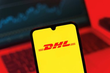 Prag, Çek Cumhuriyeti - 08 12 2025: Bilgisayarın önünde duran bir cep telefonu DHL logosunu gösteriyor. DHL uluslararası nakliye hizmeti sunan bir lojistik şirketidir..