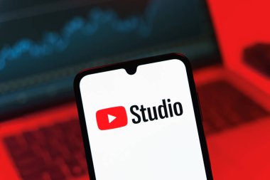 Prag, Çek Cumhuriyeti - 08 12 2025: Bir dizüstü bilgisayarın önünde duran bir cep telefonu Youtube Stüdyo logosunu gösteriyor. Youtube Studio YouTube kanallarını yönetmek ve analiz etmek için bir platformdur.