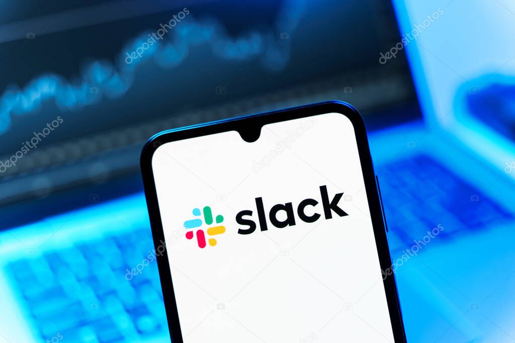 Prague, Czechia - 08 12 2025: A mobile phone standing in front of a laptop displays the Slack logo. Slack is a platform for team messaging and workplace communication.