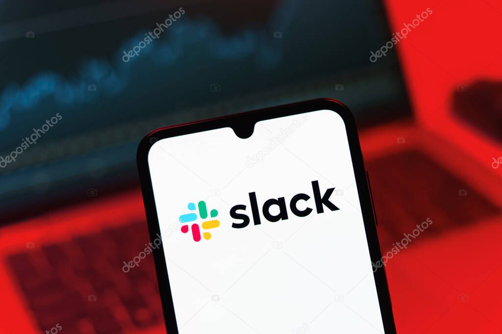 Prague, Czechia - 08 12 2025: A mobile phone standing in front of a laptop displays the Slack logo. Slack is a platform for team messaging and workplace communication.