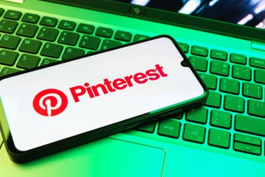 Prag, Çek Cumhuriyeti - 08 01 2025: Dizüstü bilgisayarın üzerinde duran bir cep telefonu Pinterest logosunu gösteriyor. Pinterest fikirleri görsel olarak keşfetmek ve kaydetmek için bir platformdur..