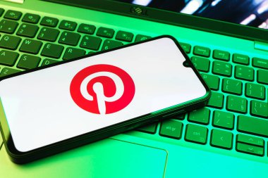 Prag, Çek Cumhuriyeti - 08 01 2025: Dizüstü bilgisayarın üzerinde duran bir cep telefonu Pinterest logosunu gösteriyor. Pinterest fikirleri görsel olarak keşfetmek ve kaydetmek için bir platformdur..