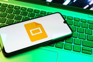 Prag, Çek Cumhuriyeti - 08 01 2025: Laptop klavyesinde duran bir cep telefonu Google Slides logosunu görüntüler. Google Slides sunumlar ve slayt gösterileri oluşturmak için bir platformdur.