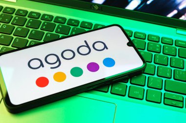 Prag, Çek Cumhuriyeti - 08 01 2025: Dizüstü bilgisayarın üzerinde duran bir cep telefonu Agoda logosunu gösteriyor. Agoda, otelleri ve seyahat yerlerini ayırtmak için bir platform..