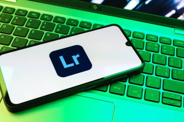 Prag, Çek Cumhuriyeti - 08 01 2025: Dizüstü bilgisayarın üzerinde duran bir cep telefonu Lightroom logosunu gösteriyor. Lightroom fotoğraf düzenleme ve yönetim için bir yazılımdır..