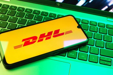 Prag, Çek Cumhuriyeti - 08 01 2025: Dizüstü bilgisayarın üzerinde duran bir cep telefonu DHL logosunu gösterir. DHL uluslararası nakliye hizmeti sunan bir lojistik şirketidir..