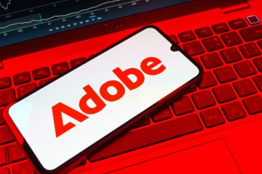 Prag, Çek Cumhuriyeti - 08 18 2025: Klavyede bir cep telefonu Adobe logosu sergiler. Adobe yaratıcı araçlar ve hizmetler sunan bir yazılım şirketidir..