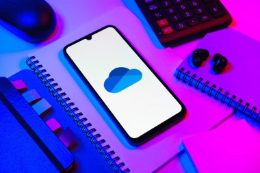 Prag, Çek Cumhuriyeti - 08 18 2025: Merkezde OneDrive logosunu gösteren bir cep telefonu ile ofis malzemeleri düzenlemesi. OneDrive dosyaları kaydetmek ve paylaşmak için bir bulut depolama platformudur.