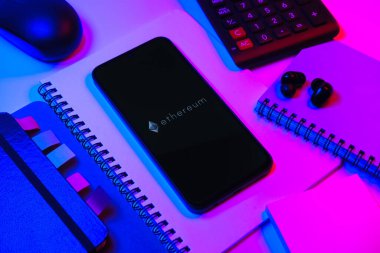 Prag, Çek Cumhuriyeti - 08 18 2025: Merkezinde Ethereum logosu bulunan bir cep telefonu ile ofis malzemeleri düzenlemesi. Ethereum merkezi olmayan uygulamalar ve kripto için bir engelleme platformudur..