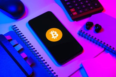 Prag, Çek Cumhuriyeti - 08 18 2025: Merkezde Bitcoin logosu sergilenen bir cep telefonu ile ofis malzemeleri düzenlemesi. Bitcoin merkezi olmayan işlemler için dijital bir kripto para birimidir.