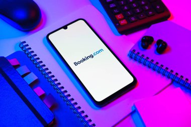 Prag, Çek Cumhuriyeti - 08 18 2025: Merkezde Booking.com logosu sergilenen bir cep telefonu ile ofis malzemeleri düzenlemesi. Rezervasyon, otel bulmak ve rezervasyon yaptırmak için bir platformdur..