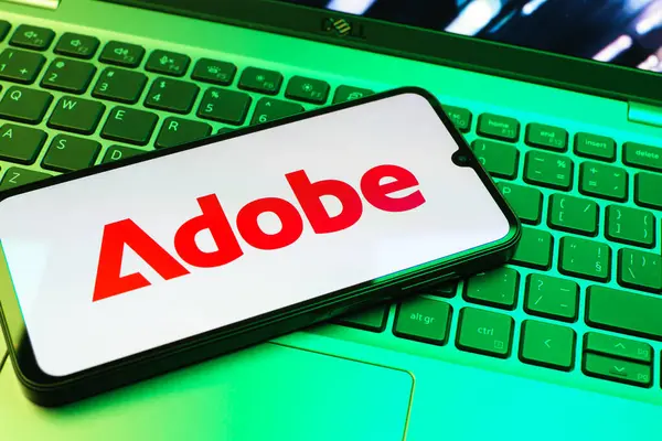 Prag, Çek Cumhuriyeti - 08 01 2025: Dizüstü bilgisayarın üzerinde duran bir cep telefonu Adobe logosunu gösterir. Adobe yaratıcı araçlar ve hizmetler sunan bir yazılım şirketidir..
