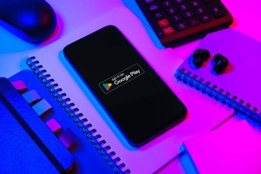 Prag, Çek Cumhuriyeti - 08 18 2025: Merkezde Google Play logosunu gösteren bir cep telefonu ile ofis malzemeleri düzenlemesi. Google Play uygulamaları, oyunları ve dijital içeriği indirmek için bir platformdur.