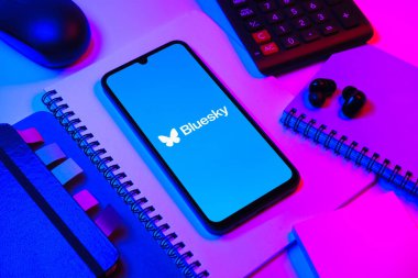 Prag, Çek Cumhuriyeti - 08 18 2025: Merkezde Bluesky logosunu gösteren bir cep telefonu ile ofis malzemeleri düzenlemesi. Bluesky merkezi olmayan ağlar için bir sosyal medya platformudur..
