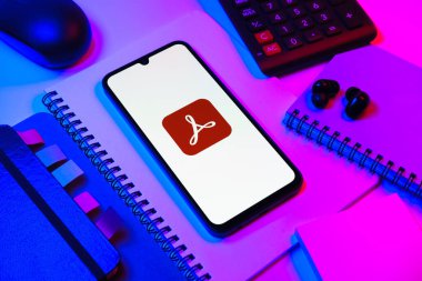 Prag, Çek Cumhuriyeti - 08 18 2025: Merkezinde Acrobat Reader logosu bulunan bir cep telefonu ile ofis malzemeleri düzenlemesi. Acrobat Reader, PDF belgelerini görüntülemek ve yönetmek için bir platformdur.