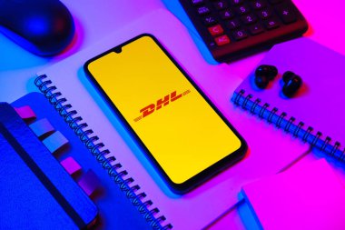 Prag, Çek Cumhuriyeti - 08 18 2025: Merkezde DHL logosu sergilenen bir cep telefonu ile ofis malzemeleri düzenlemesi. DHL uluslararası nakliye hizmeti sunan bir lojistik şirketidir..