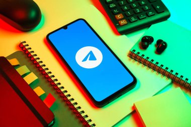 Prag, Çek Cumhuriyeti - 08 18 2025: Merkezde Telegram logosunu gösteren bir cep telefonu ile ofis malzemeleri düzenlemesi. Telgraf hızlı ve güvenli iletiler için bir uygulamadır.