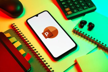 Prag, Çek Cumhuriyeti - 08 18 2025: Merkezde Powerpoint logosunu gösteren bir cep telefonu ile ofis malzemeleri düzenlemesi. Powerpoint sunumlar ve slayt gösterileri oluşturmak için bir yazılımdır..