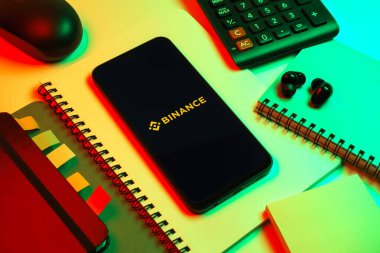 Prag, Çek Cumhuriyeti - 08 18 2025: Merkezde Binance logosunu gösteren bir cep telefonu ile ofis malzemeleri düzenlemesi. Binance dijital varlıkların ticareti için bir kripto para değiş tokuşu.