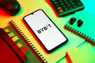 Prag, Çek Cumhuriyeti - 08 18 2025: Merkezde Bybit logosunu gösteren bir cep telefonu ile ofis malzemeleri düzenlemesi. Bybit şifreli para ve türev ticareti için bir platformdur.