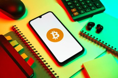 Prag, Çek Cumhuriyeti - 08 18 2025: Merkezde Bitcoin logosu sergilenen bir cep telefonu ile ofis malzemeleri düzenlemesi. Bitcoin merkezi olmayan işlemler için dijital bir kripto para birimidir.