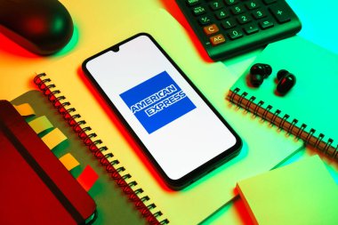 Prag, Çek Cumhuriyeti - 08 18 2025: Merkezde American Express logosunu gösteren bir cep telefonu ile ofis malzemeleri düzenlemesi. American Express kart ve bankacılık sunan bir finans şirketidir..