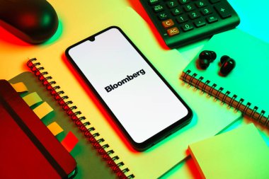 Prag, Çek Cumhuriyeti - 08 18 2025: Merkezde Bloomberg logosunu gösteren bir cep telefonu ile ofis malzemeleri düzenlemesi. Bloomberg finansal haberler, veriler ve analizler sağlayan bir şirkettir..