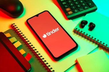 Prag, Çek Cumhuriyeti - 08 18 2025: Merkezde Tinder logosu sergilenen bir cep telefonu ile ofis malzemeleri düzenlemesi. Tinder insanları eşleştirmek ve bağlamak için bir randevu uygulaması.