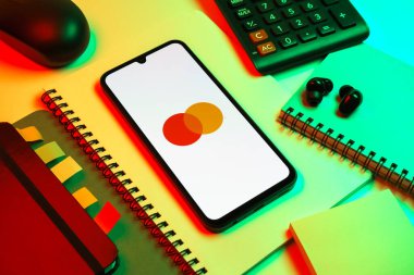 Prag, Çek Cumhuriyeti - 08 18 2025: Merkezde Mastercard logosu sergilenen bir cep telefonu ile ofis malzemeleri düzenlemesi. Mastercard ödeme kartları ve hizmetler sağlayan bir finans şirketidir..