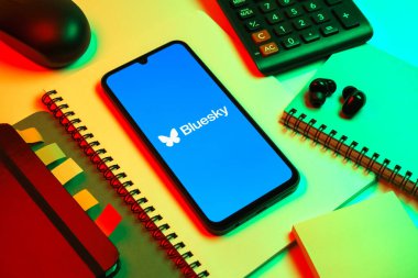 Prag, Çek Cumhuriyeti - 08 18 2025: Merkezde Bluesky logosunu gösteren bir cep telefonu ile ofis malzemeleri düzenlemesi. Bluesky merkezi olmayan ağlar için bir sosyal medya platformudur..