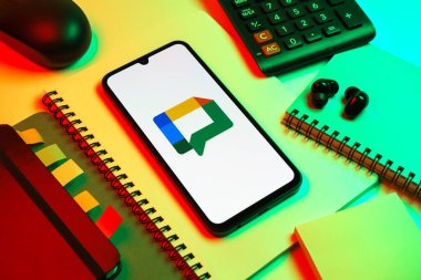 Prag, Çek Cumhuriyeti - 08 18 2025: Merkezde Google Chat logosunu gösteren bir cep telefonu ile ofis malzemeleri düzenlemesi. Google Chat mesajlaşma ve takım işbirliği için bir platformdur.
