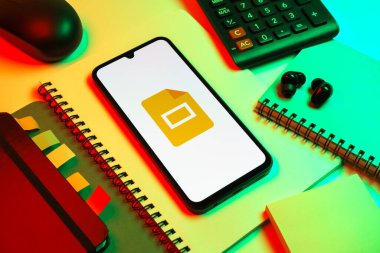 Prag, Çek Cumhuriyeti - 08 18 2025: Merkezde Google Slides logosunu gösteren bir cep telefonu ile ofis malzemeleri düzenlemesi. Google Slides sunumlar ve slayt gösterileri oluşturmak için bir platformdur.