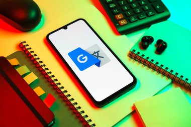 Prag, Çek Cumhuriyeti - 08 18 2025: Merkezde Google Translate logosunu gösteren bir cep telefonu ile ofis malzemeleri düzenlemesi. Google Çevirisi metni ve konuşmayı diller arası çevirmek için bir platformdur..