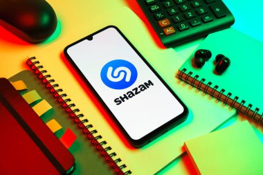 Prag, Çek Cumhuriyeti - 08 18 2025: Merkezinde Shazam logosu bulunan bir cep telefonu ile ofis malzemeleri düzenlemesi. Shazam şarkıları ve müzik parçalarını tanımlamak için bir uygulamadır.