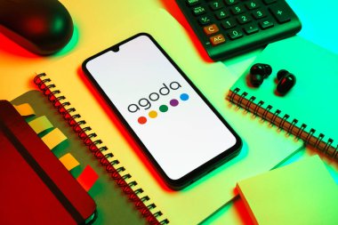 Prag, Çek Cumhuriyeti - 08 18 2025: Merkezde Agoda logosunu gösteren bir cep telefonu ile ofis malzemeleri düzenlemesi. Agoda, otelleri ve seyahat yerlerini ayırtmak için bir platform..