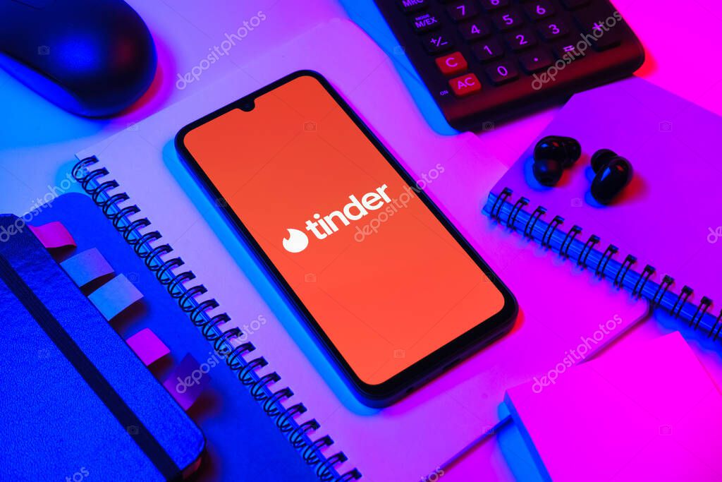 Prague, Czechia - 08 18 2025: An arrangement of office supplies with a mobile phone in the center displaying Tinder logo. Tinder is a dating app for matching and connecting people.