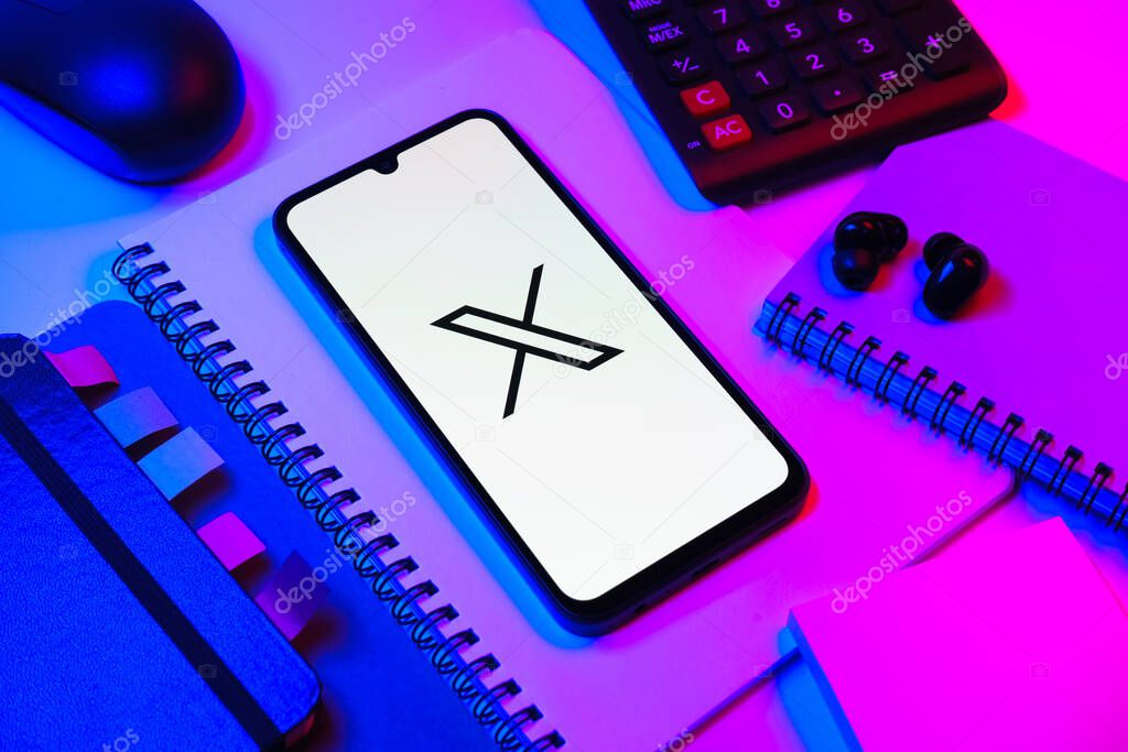 Prague, Czechia - 08 18 2025: An arrangement of office supplies with a mobile phone in the center displaying X logo. X is a platform for sharing short posts and updates.