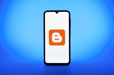Prag, Çek Cumhuriyeti - 08 10 2025: Tek bir arkaplanda duran bir cep telefonu Blogger logosunu gösterir. Blogger blog oluşturma ve yayınlama için bir platformdur.