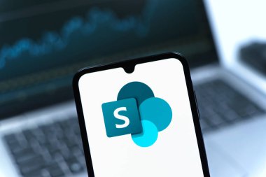 Prag, Çek Cumhuriyeti - 08 12 2025: Bilgisayarın önünde duran bir cep telefonu Microsoft Sharepoint logosunu gösteriyor. Microsoft Sharepoint işbirliği ve belge yönetimi için bir platformdur.
