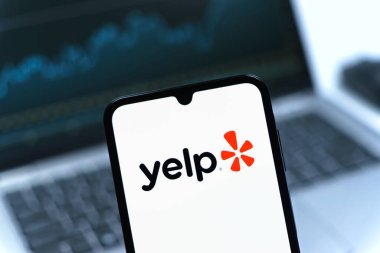 Prag, Çek Cumhuriyeti - 08 12 2025: Laptopun önünde duran bir cep telefonu Yelp logosunu gösteriyor. Yelp yerel işletmeleri bulmak ve incelemek için bir platformdur.