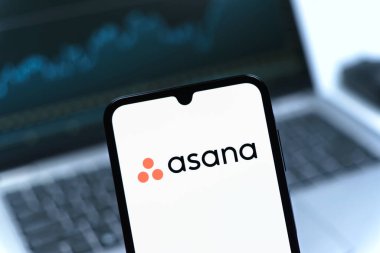 Prag, Çek Cumhuriyeti - 08 12 2025: Bilgisayarın önünde duran bir cep telefonu Asana logosunu gösteriyor. Asana görev yönetimi ve takım işbirliği için bir platformdur..