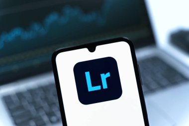 Prag, Çek Cumhuriyeti - 08 12 2025: Dizüstü bilgisayarın önünde duran bir cep telefonu Lightroom logosunu gösteriyor. Lightroom fotoğraf düzenleme ve yönetim için bir yazılımdır..