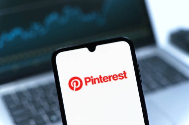 Prag, Çek Cumhuriyeti - 08 12 2025: Bilgisayarın önünde duran bir cep telefonu Pinterest logosunu gösteriyor. Pinterest fikirleri görsel olarak keşfetmek ve kaydetmek için bir platformdur..