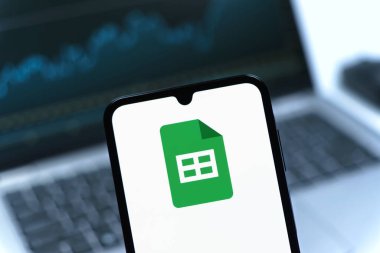 Prag, Çek Cumhuriyeti - 08 12 2025: Bir dizüstü bilgisayarın önünde duran bir cep telefonu Google Sheets logosunu görüntüler. Google Sayfalar tablo oluşturmak ve yönetmek için bir platformdur.