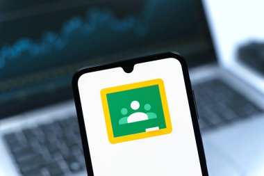 Prag, Çek Cumhuriyeti - 08 12 2025: Bir dizüstü bilgisayarın önünde duran bir cep telefonu Google Sınıfı logosunu gösteriyor. Google Sınıfı, sınıfları ve eğitim içeriğini yönetmek için bir platformdur.