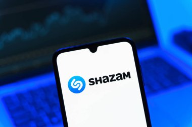 Prag, Çek Cumhuriyeti - 08 12 2025: Dizüstü bilgisayarın önünde duran bir cep telefonu Shazam logosunu gösteriyor. Shazam şarkıları ve müzik parçalarını tanımlamak için bir uygulamadır.