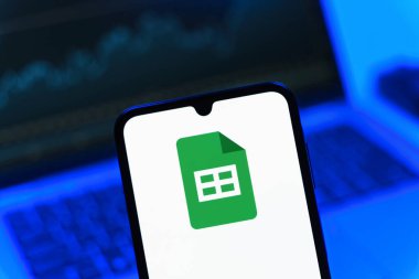 Prag, Çek Cumhuriyeti - 08 12 2025: Bir dizüstü bilgisayarın önünde duran bir cep telefonu Google Sheets logosunu görüntüler. Google Sayfalar tablo oluşturmak ve yönetmek için bir platformdur.