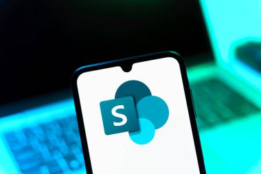 Prag, Çek Cumhuriyeti - 08 12 2025: Bilgisayarın önünde duran bir cep telefonu Microsoft Sharepoint logosunu gösteriyor. Microsoft Sharepoint işbirliği ve belge yönetimi için bir platformdur.